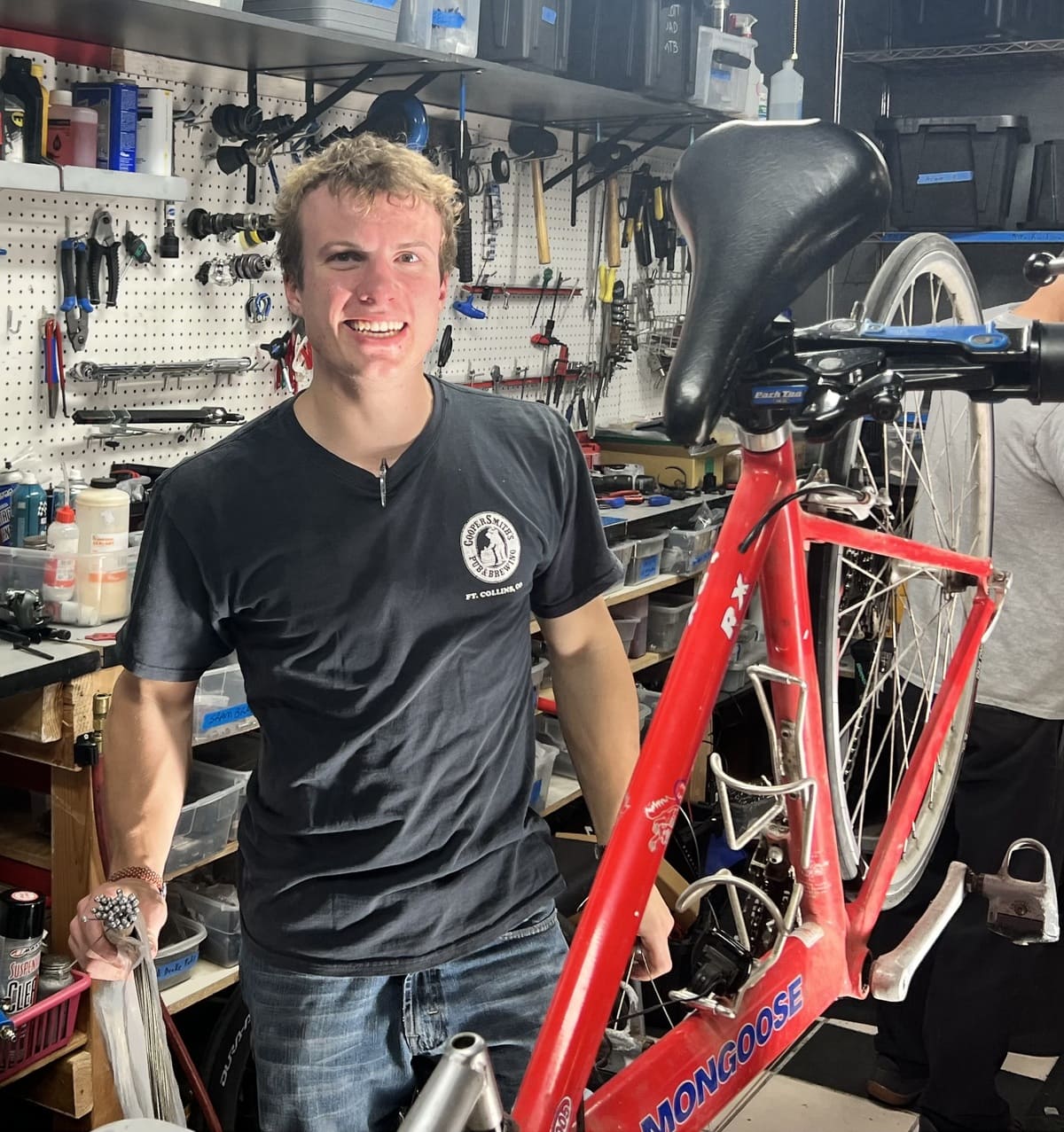 Person standing next to a red bicycle in a workshop with tools and equipment on shelves.