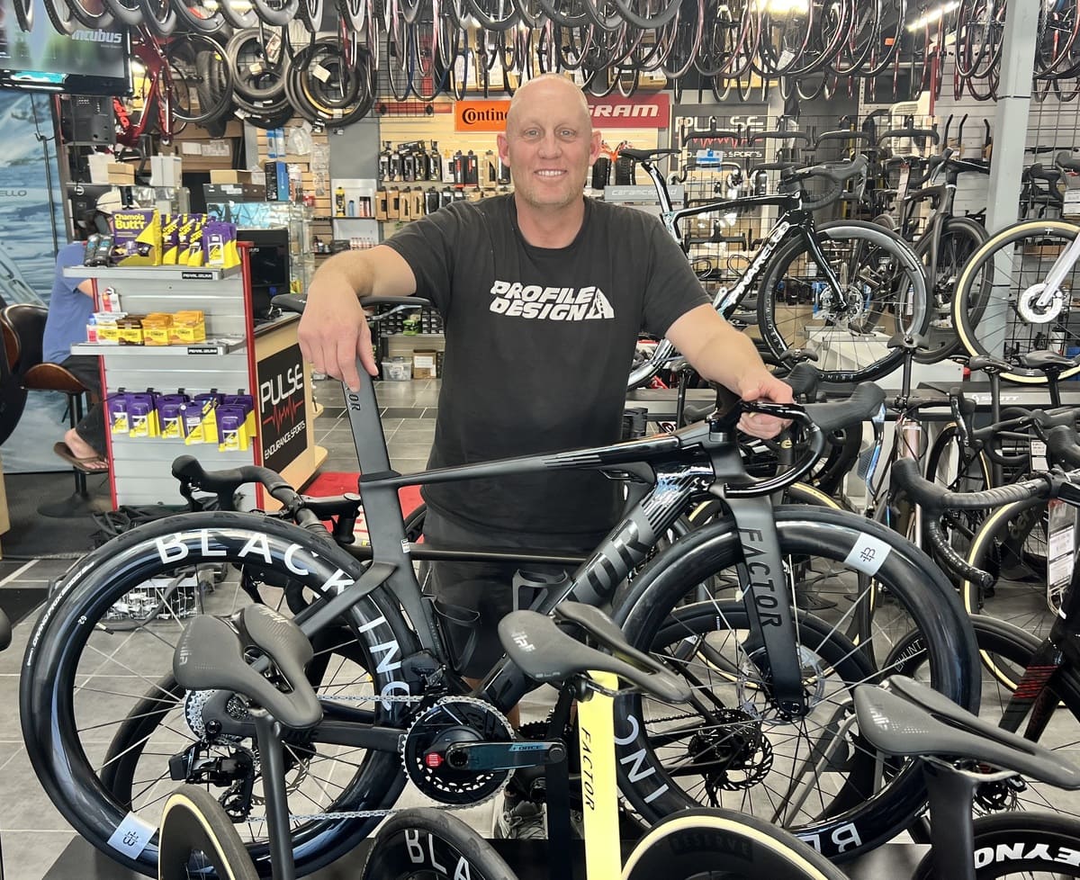 Man holding a bicycle in a bike shop with various bikes and products in the background